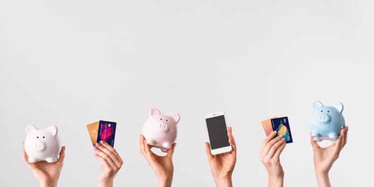 Female hands with credit cards, piggy banks and mobile phone on light background